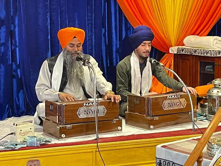 Two ragis playing harmonium and singing kirtan inside the Gurdwara