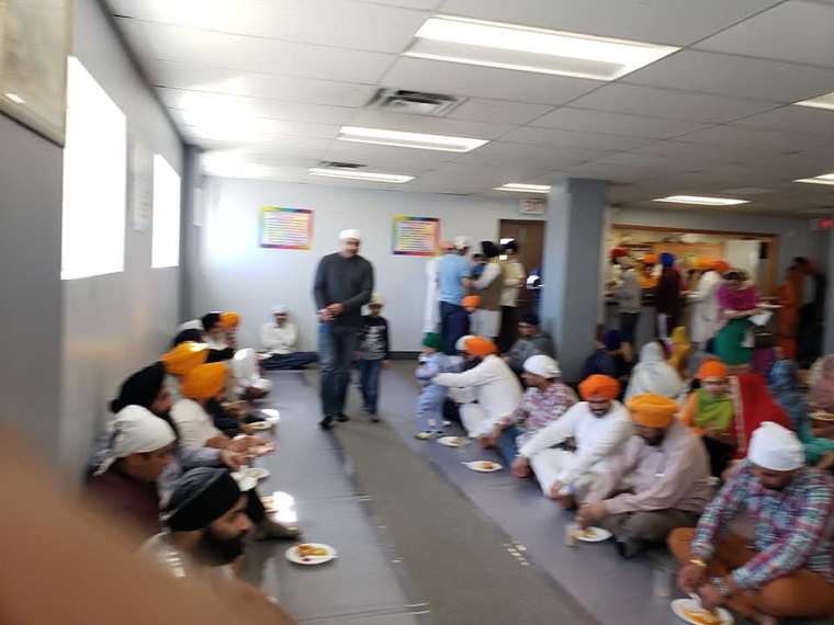 Members of the community sitting together on the floor sharing the free langar meal