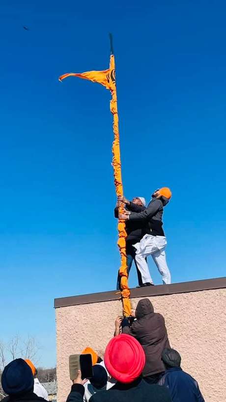 Volunteers raising the Nishan Sahib, the Sikh flag, against a clear blue sky
